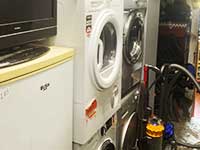 side angled photo of appliances including 4 white coloured washing machines for sale next to a fridge and a hoover to buy