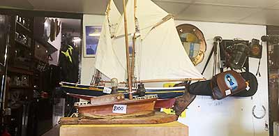 close up photo of bric a brac items and a medium sized light coloured wood model ship complete with masts and white sails made from wood and delicately painted