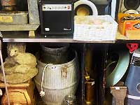 close up center view of an old metal barrel with some rust and lots of age next to a paraffin heater and garden ornaments such as an otter and a lion