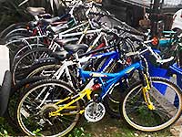 a row of secondhand scooters and bikes for sale in many different colours including blue red green and orange in varying height sizes for many age groups