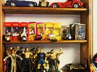 close up photo of a cabinet with lots of toys on including toy metal cars along with boxed and unboxed old retro action figures